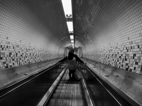 Black and White Photo of People on an Escalator in a Tunnel 