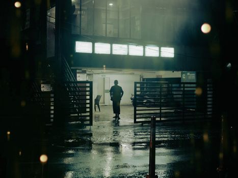 Silhouette of a person in a rainy, illuminated street scene in Hyderabad, India.