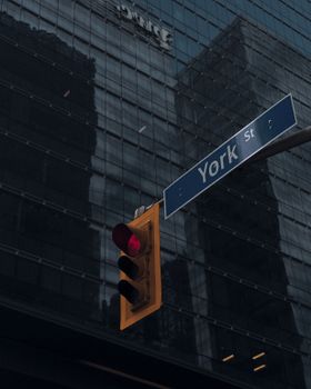 Low angle view of a York Street sign and red traffic light against a glass building in Toronto, Canada.