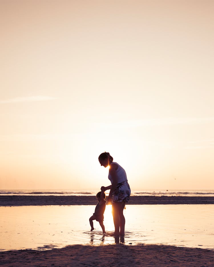 Mother With Child Playing On The Beach At Sunset