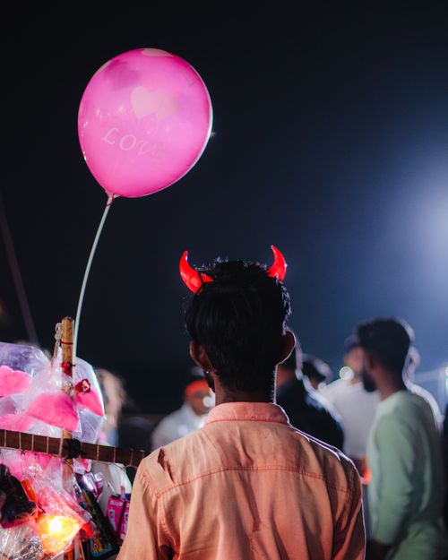 Free A festive night scene featuring a man with red devil horns and a pink balloon in a lively crowd. Stock Photo