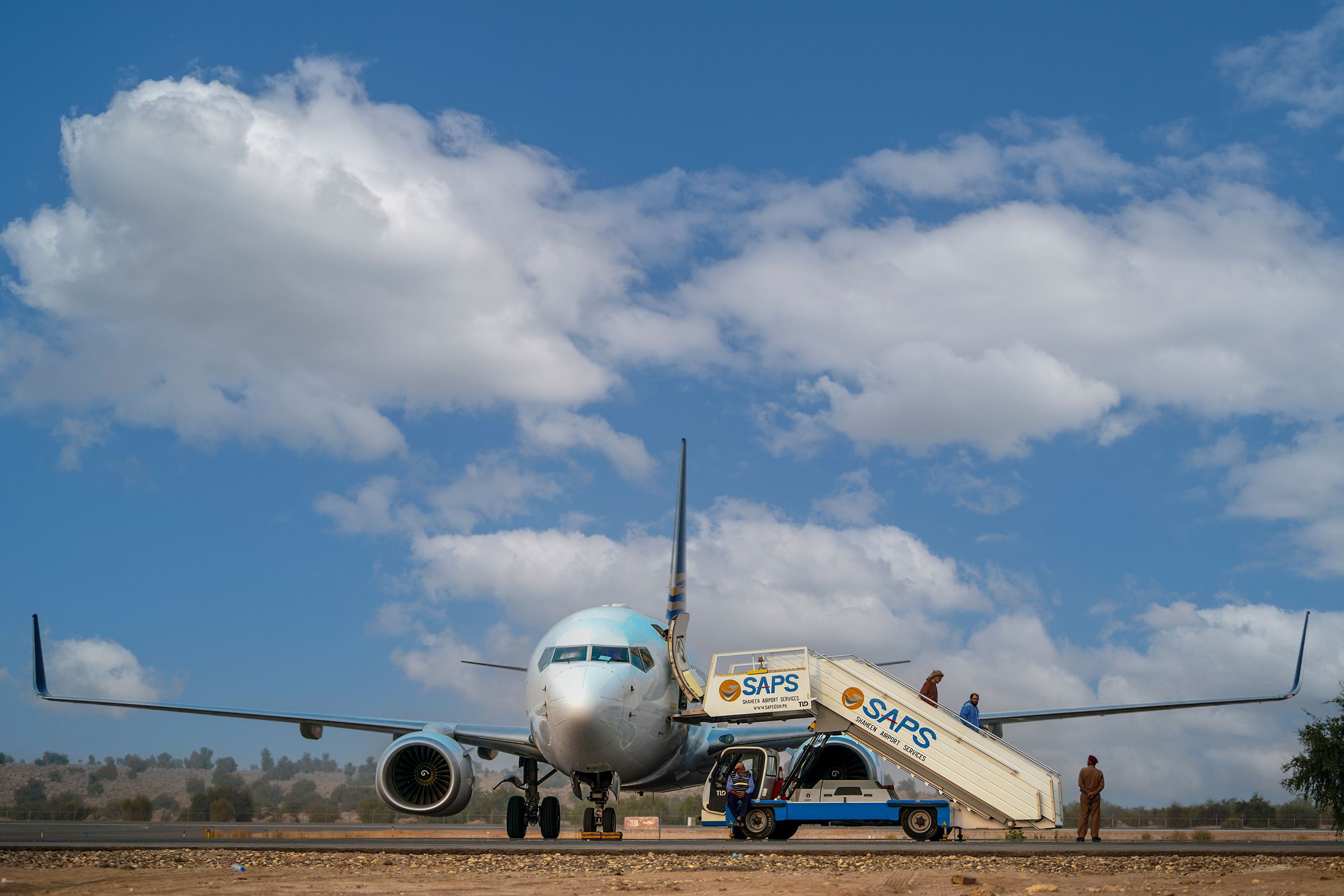 Commercial airplane on runway with boarding stairs and workers preparing for departure.