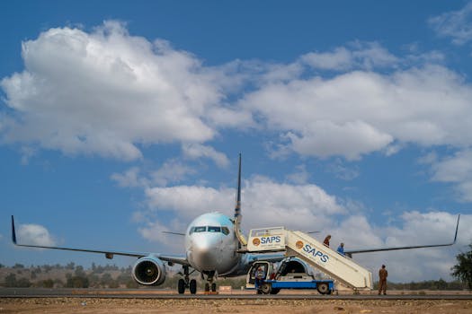 Commercial airplane on runway with boarding stairs and workers preparing for departure.