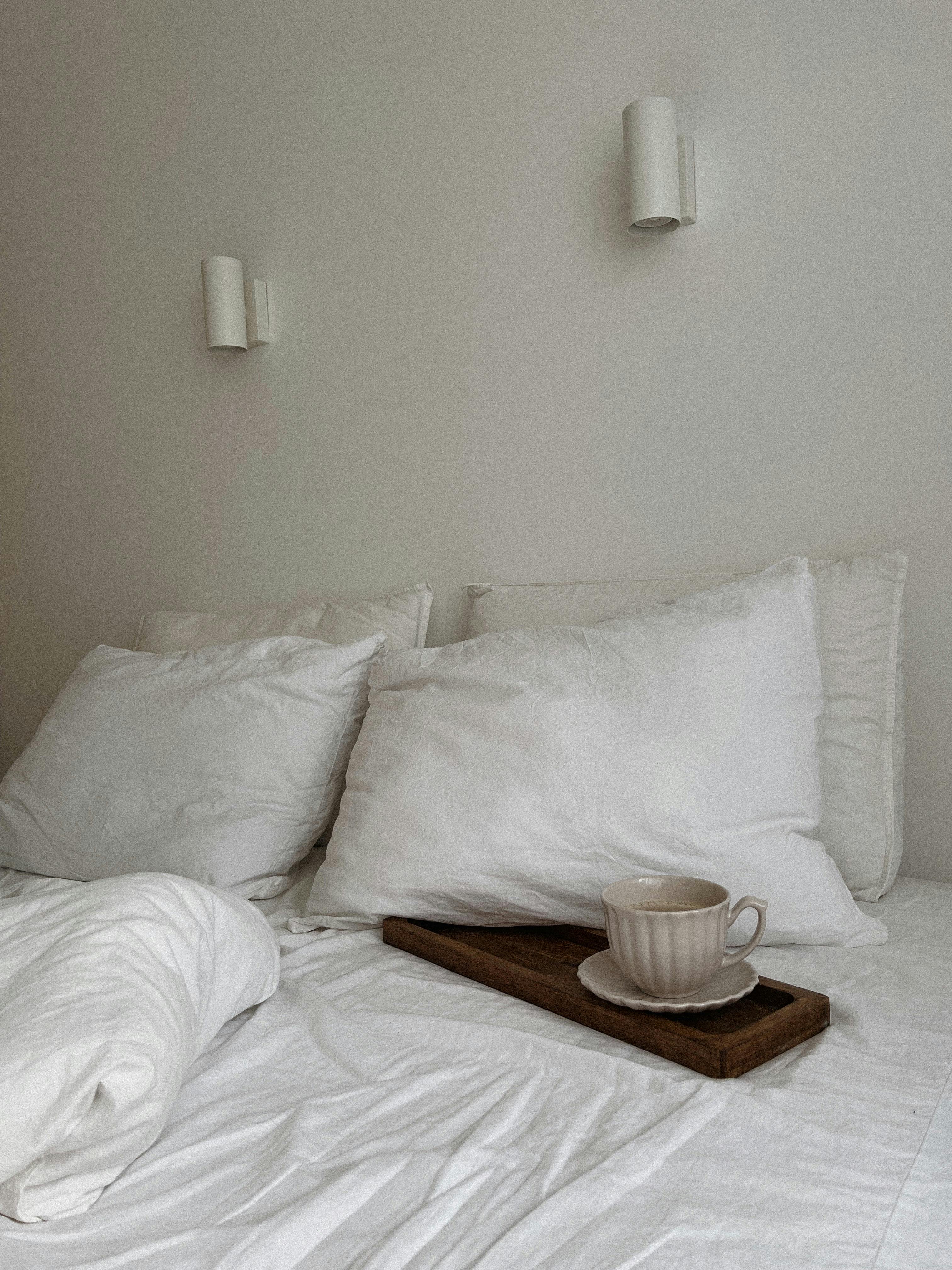 Minimalist bedroom with soft pillows and a coffee cup on a bed, perfect for a cozy lifestyle.