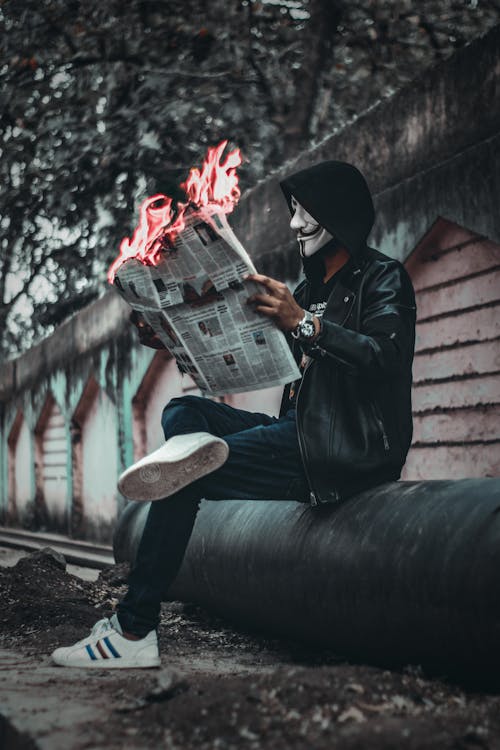 男人戴着面具坐下来，拿着报纸与火