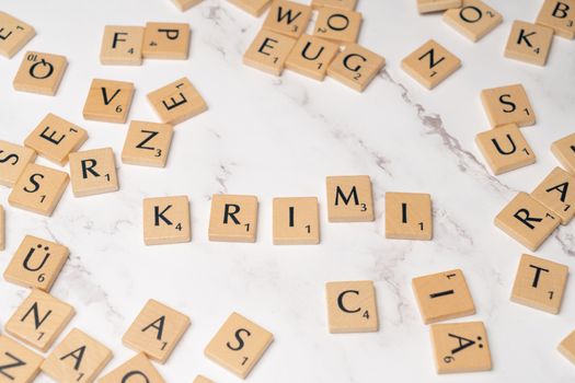 Wooden letter tiles arranged randomly on a marble background, spelling 'KRIMI'.