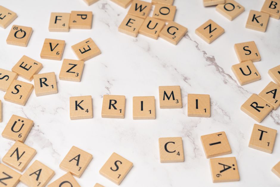 Wooden letter tiles arranged randomly on a marble background, spelling 'KRIMI'.
