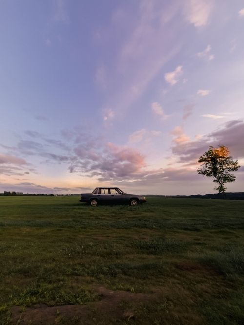 Free A lone vintage car in a tranquil green field during a colorful sunset. Stock Photo