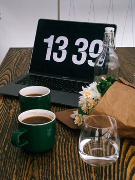 A warm workspace setting featuring coffee mugs, a laptop, flowers, and a water bottle.