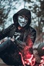 一个戴着面具、穿着夹克的神秘人物坐在户外篝火旁