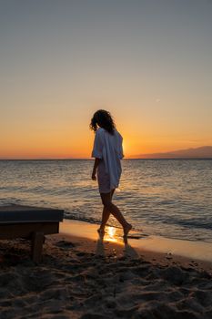 A woman strolls along Thasos' beach during a breathtaking sunset, capturing the essence of relaxation and summer.