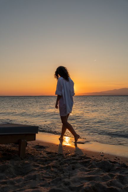 A woman strolls along Thasos' beach during a breathtaking sunset, capturing the essence of relaxation and summer.