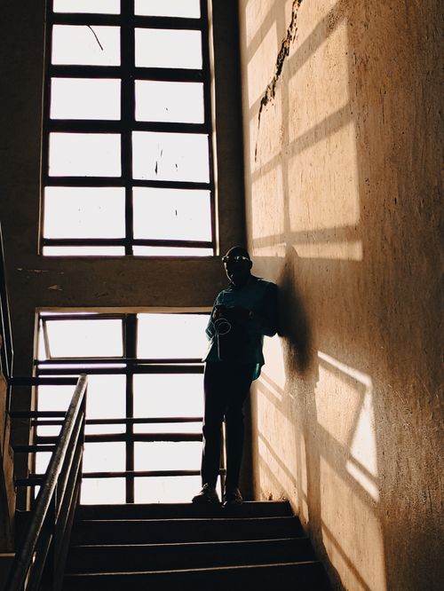 Free A person stands by windows, casting a silhouette on an indoor staircase. Stock Photo
