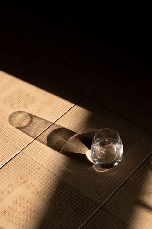 Free Minimalist scene with a glass of water casting intricate shadows on a textured sunlit floor. Stock Photo
