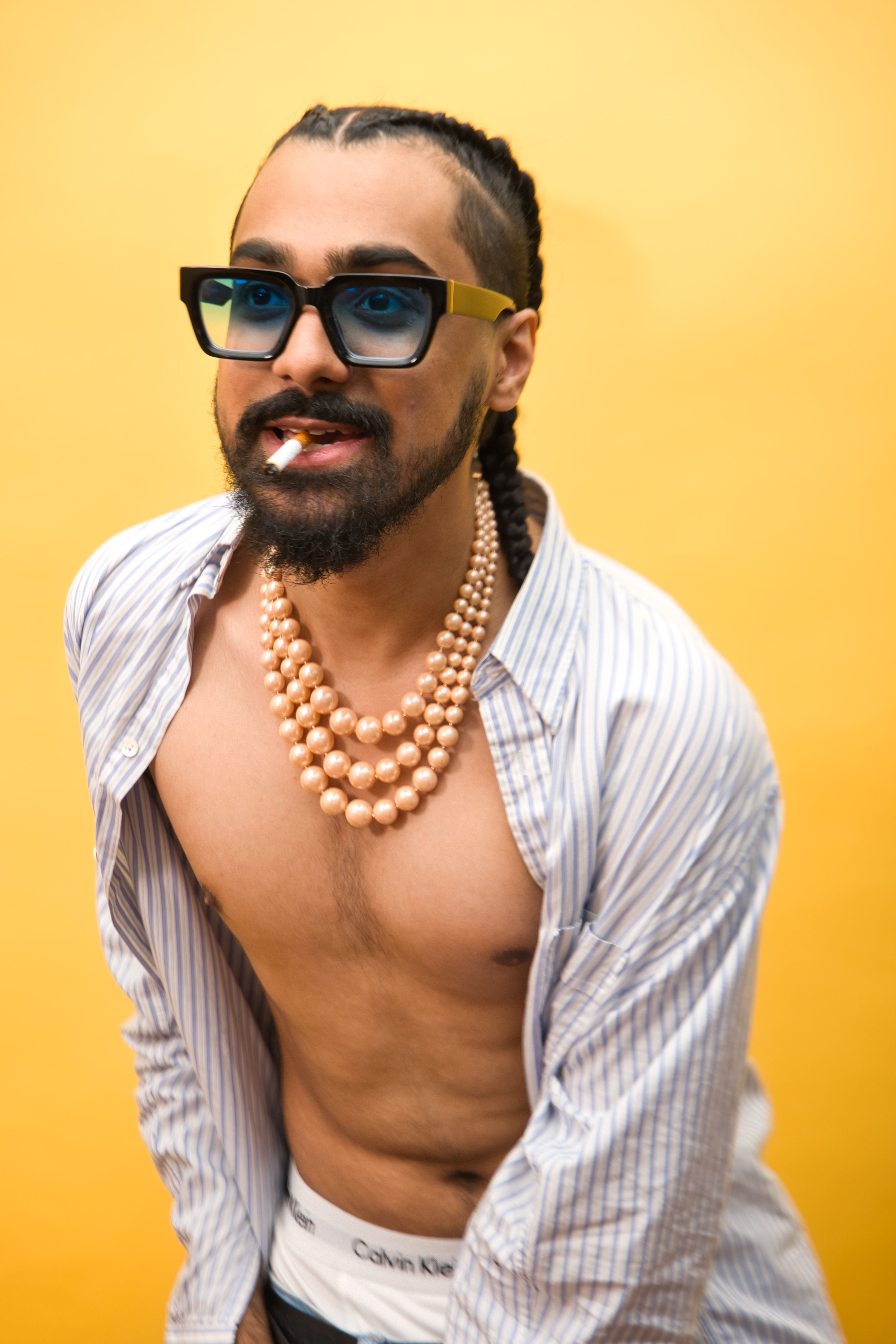 Portrait of a fashionable man with sunglasses and pearls against a yellow background.