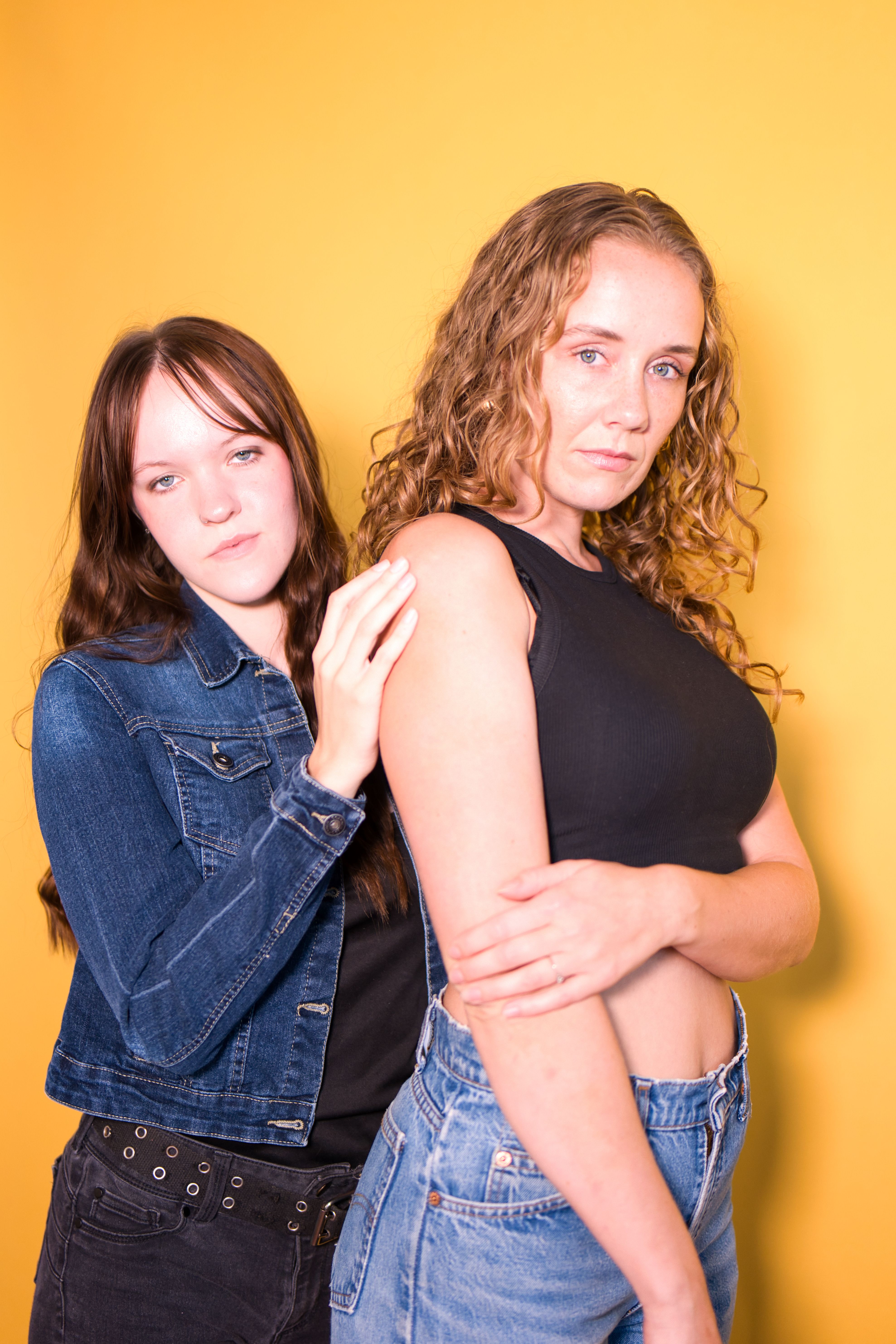 A studio portrait of two women posing confidently against a vibrant yellow background.