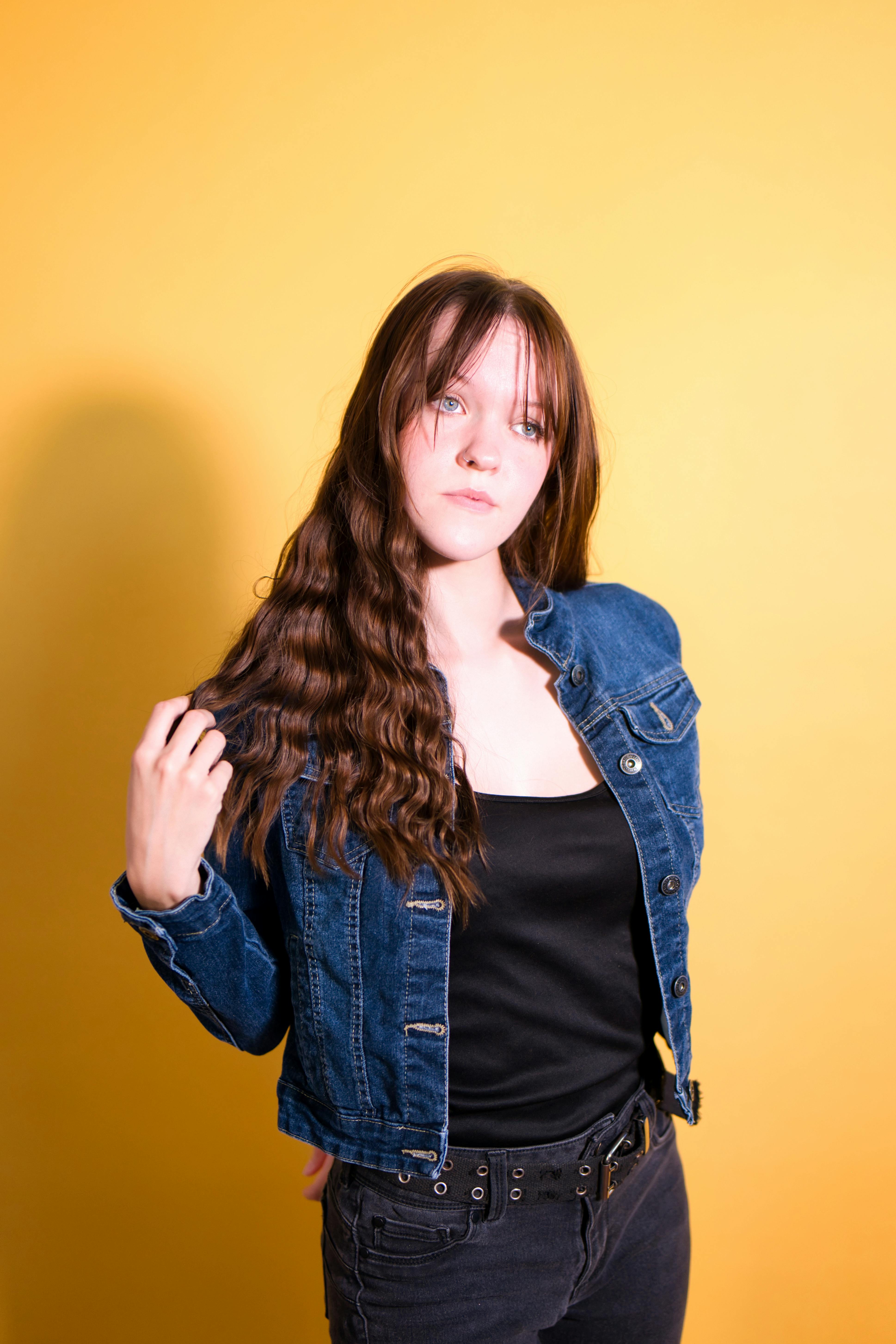 Stylish woman posing in jean jacket against vibrant yellow backdrop.