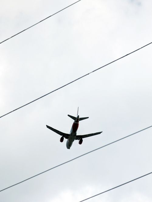Free Low-angle shot of an airplane in flight above power lines against a cloudy sky. Stock Photo