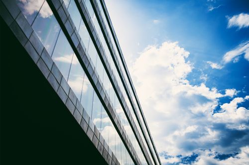 Free Low-angle view of a modern glass building reflecting a vibrant blue sky with clouds. Stock Photo