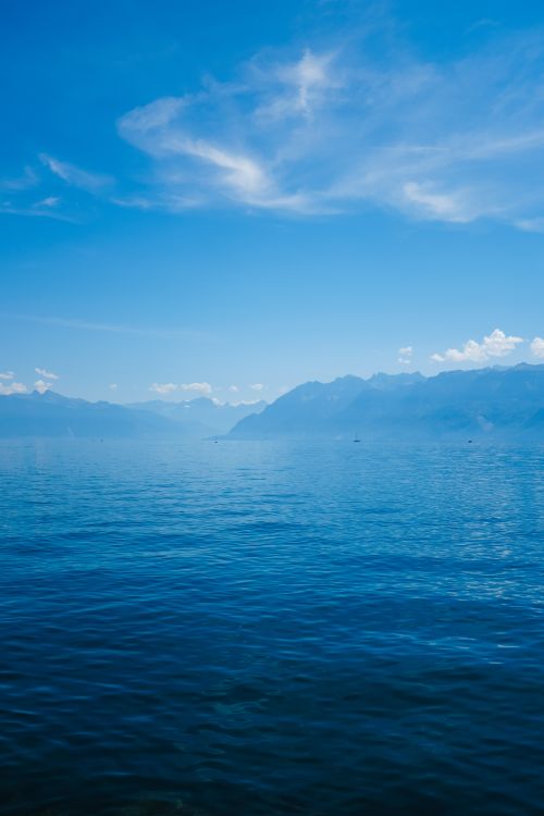 Free A serene seascape showcasing clear blue water and distant mountains under a cloudy sky. Stock Photo
