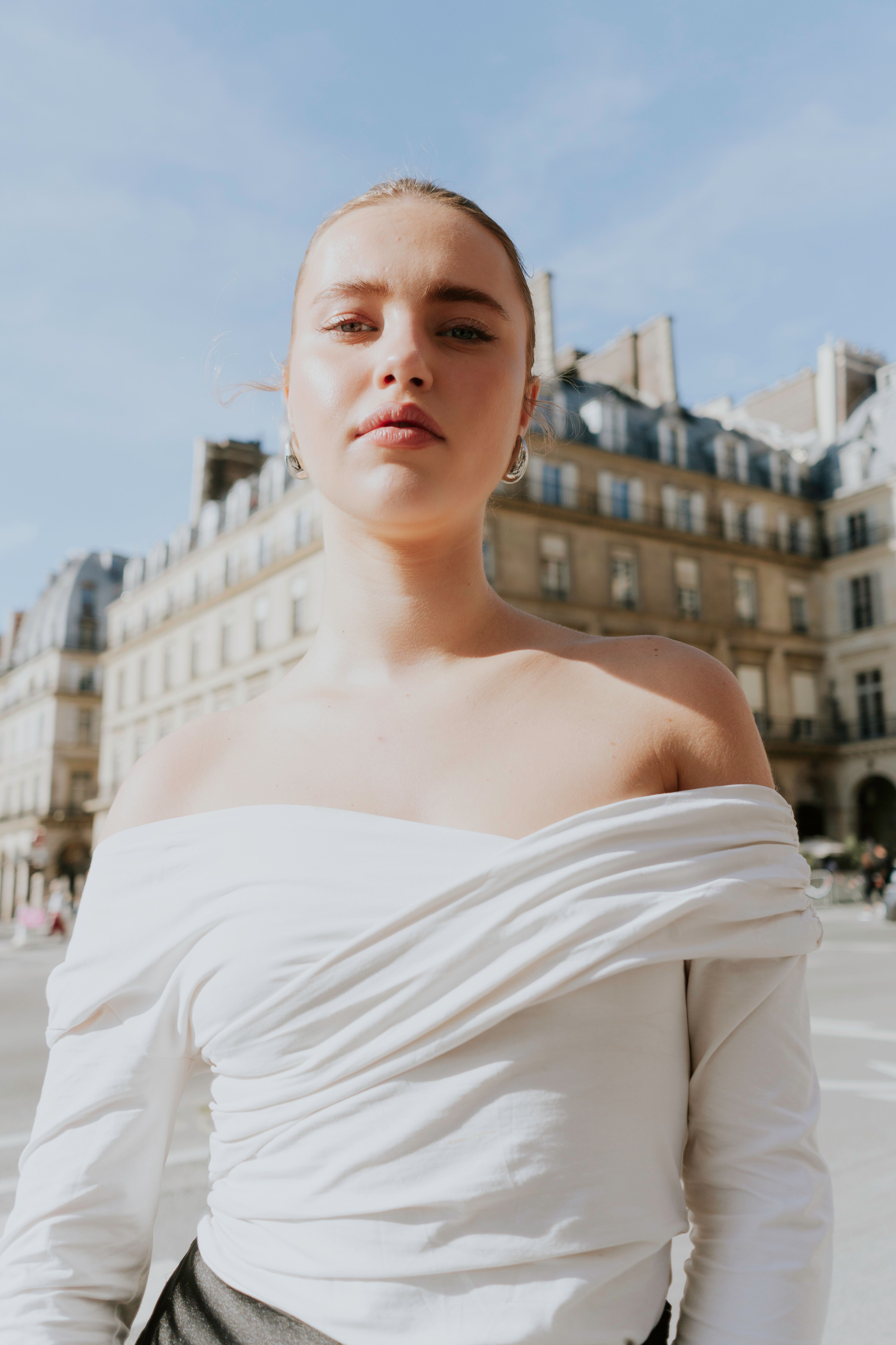 Stylish woman in white top posing in cityscape with elegant architecture backdrop.
