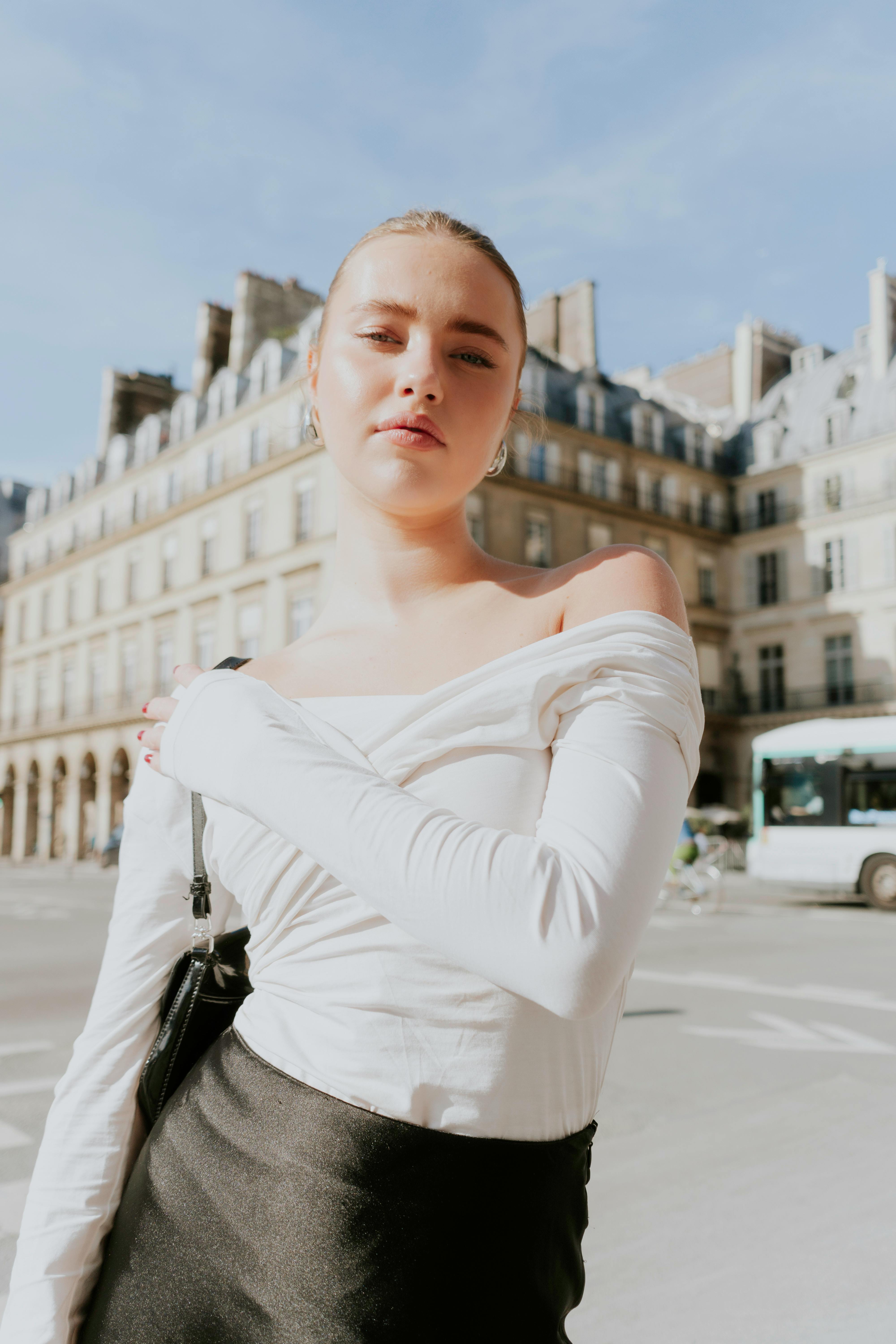 Stylish woman in white top posing confidently on a city street with historic architecture.