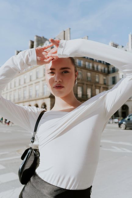 Confident young woman posing in modern fashion on a sunlit city street.