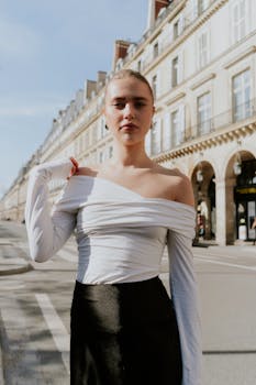 Stylish woman posing elegantly on a sunlit city street with classic architecture.