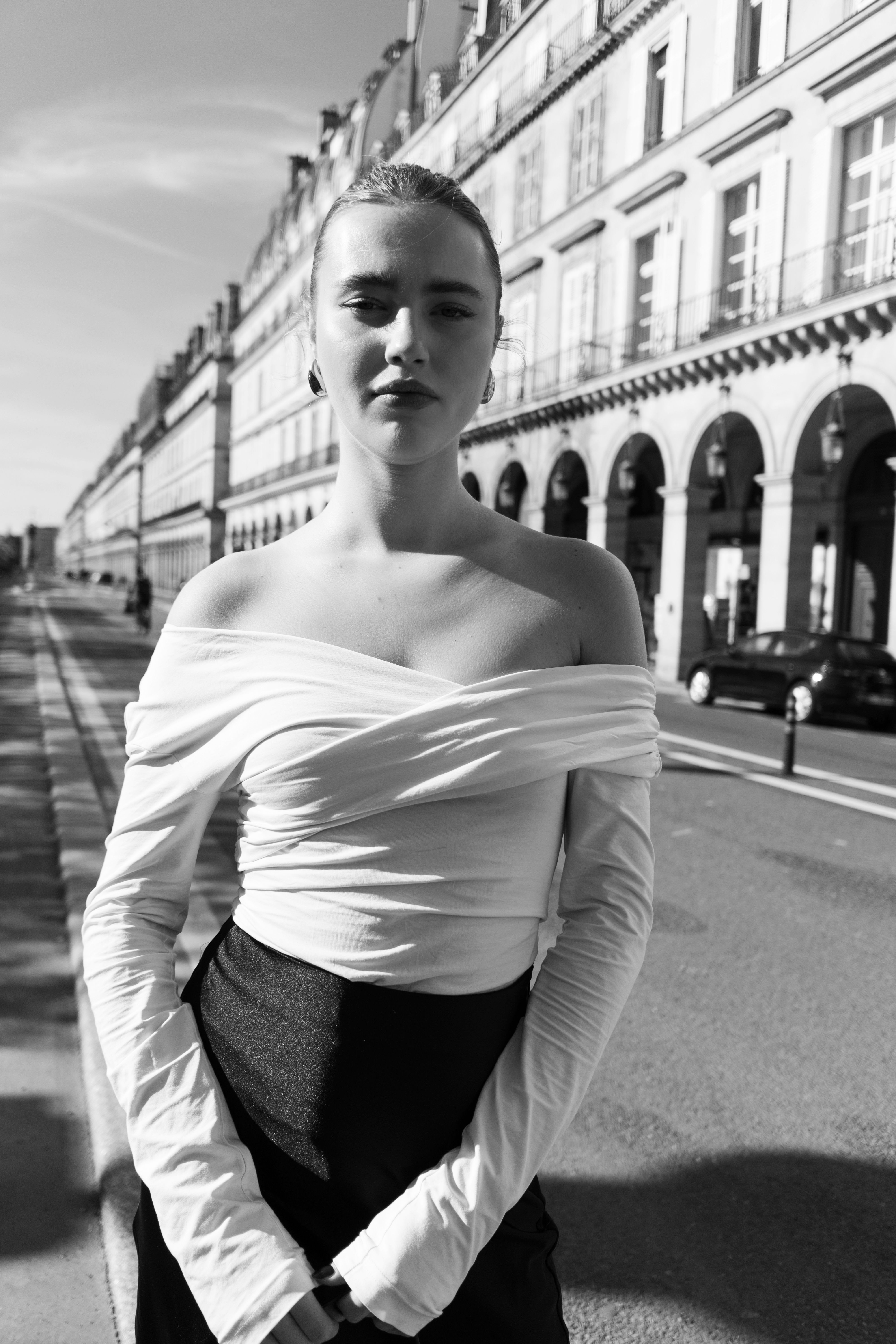 Stylish woman wearing off-shoulder dress posing confidently on city street, showcasing urban fashion.