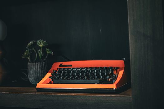 A classic orange typewriter sits on a wooden shelf with a retro vibe, highlighting vintage style.