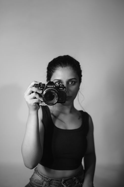 Free Black and white portrait of a female photographer holding a camera in a studio setting. Stock Photo