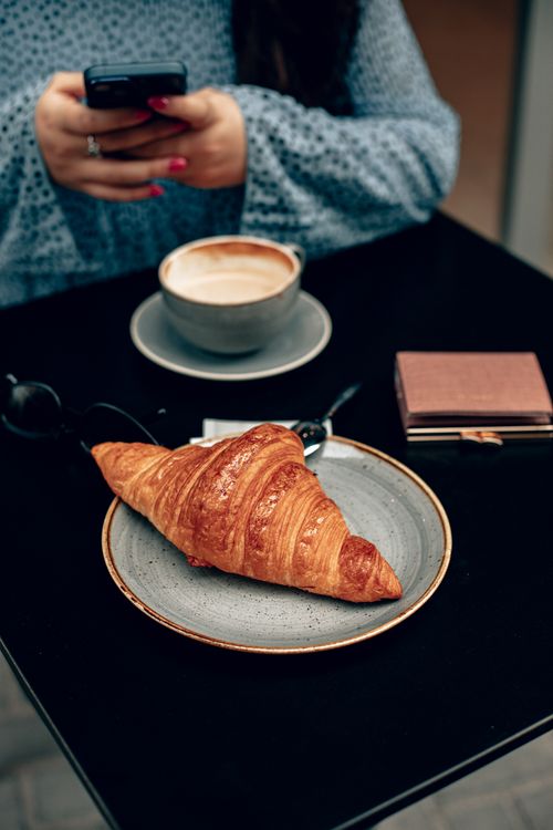 Free Woman enjoying coffee and croissant at a cafe in Baku, Azerbaijan, using smartphone. Stock Photo