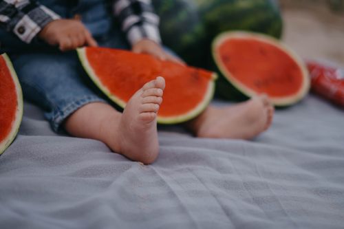 Free Adorable scene of a baby sitting with watermelon slices on a warm summer day. Stock Photo