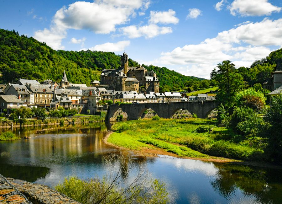 Explore the picturesque village of Estaing and its historic castle surrounded by lush greenery and a serene river.