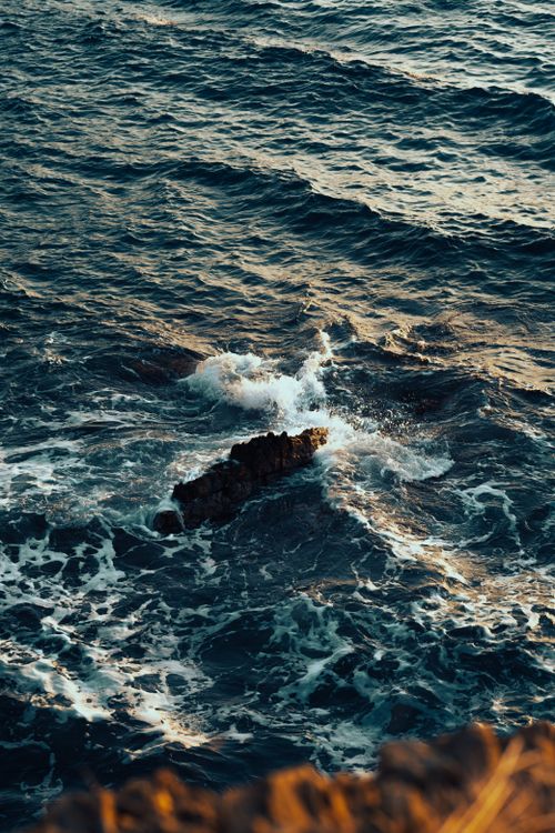 Free Captivating view of ocean waves crashing on rocky shoreline during sunset, showcasing nature's power. Stock Photo