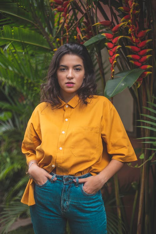 Free Standing Woman With Hands on Pockets Beside Heliconia Rostata Plants Stock Photo