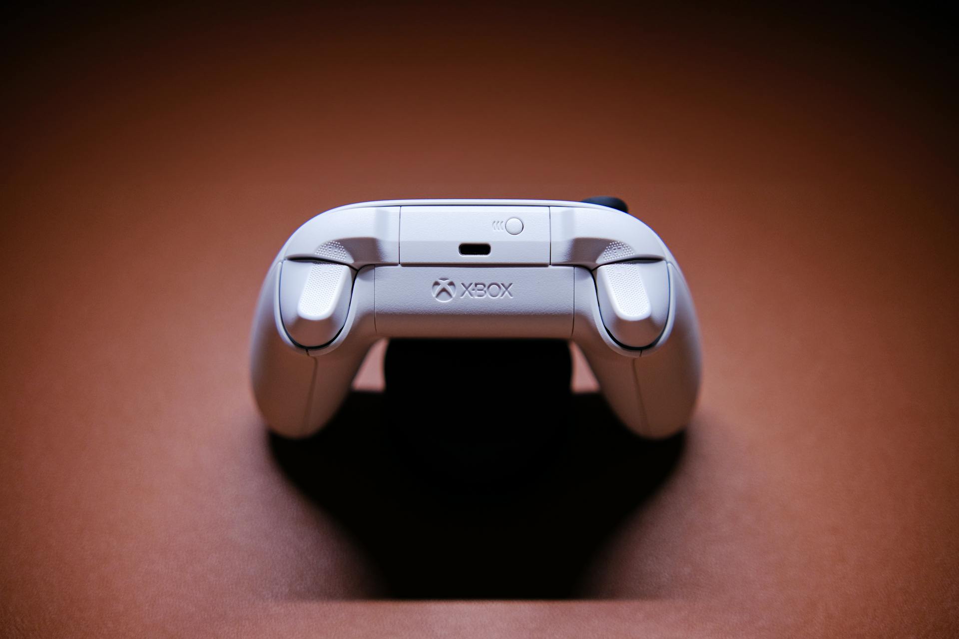 A white Xbox game controller beautifully captured on a light brown background, showcasing modern gaming technology.