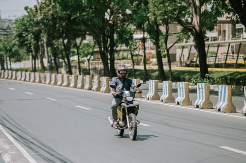 Free A motorcyclist wearing a helmet rides through an urban city street with trees and barriers. Stock Photo