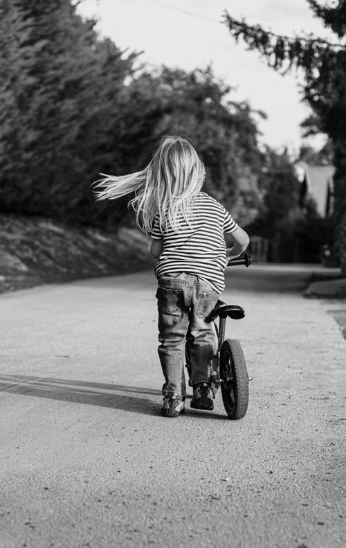 Free A carefree child riding a bicycle on a quiet countryside road, captured in black and white. Stock Photo