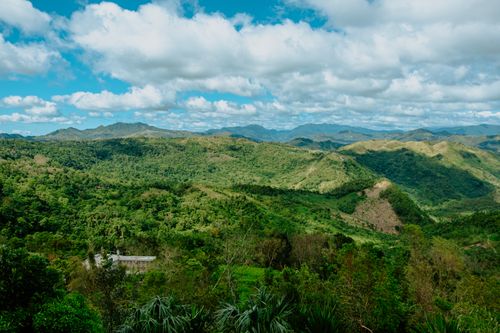 Free Expansive view of lush green mountains and valleys under a bright blue sky with clouds. Stock Photo
