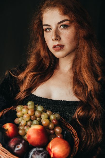 A striking portrait of a redhead woman holding a basket of fruits, exuding elegance and natural beauty.
