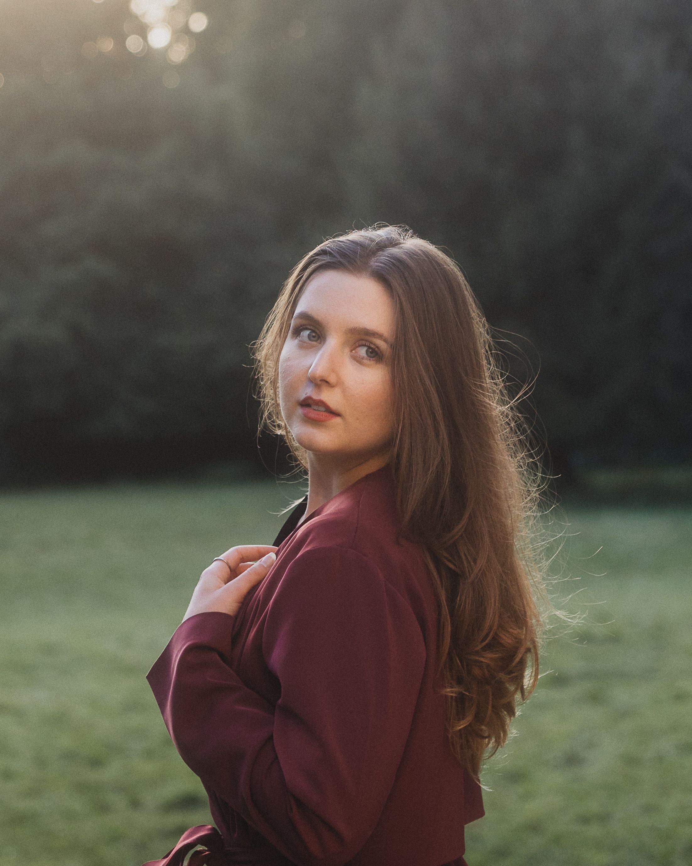 Stylish woman posing in a Berlin park at dusk in a burgundy coat.