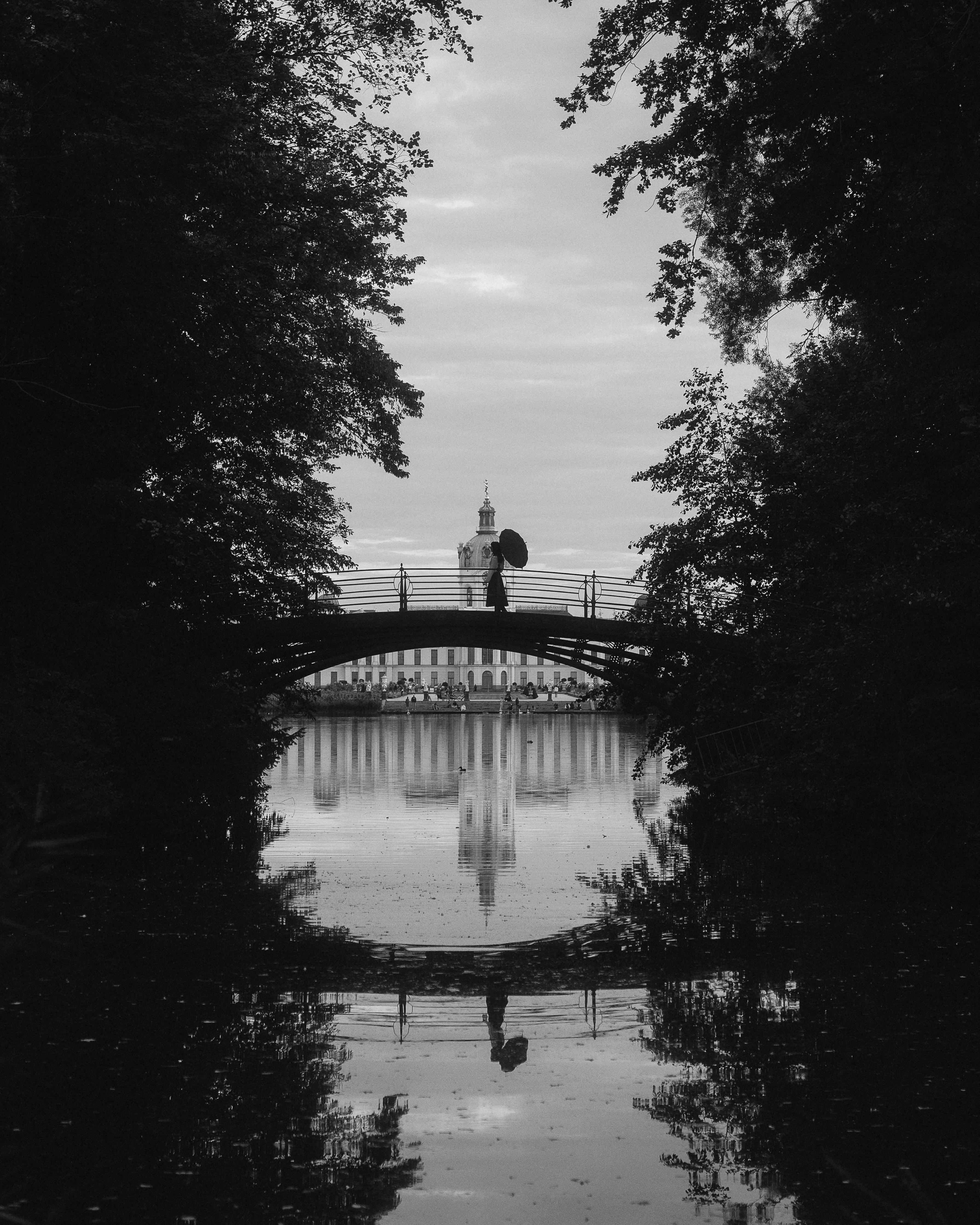 Black and white silhouette of a person with umbrella on a bridge by Charlottenburg Palace, Berlin.