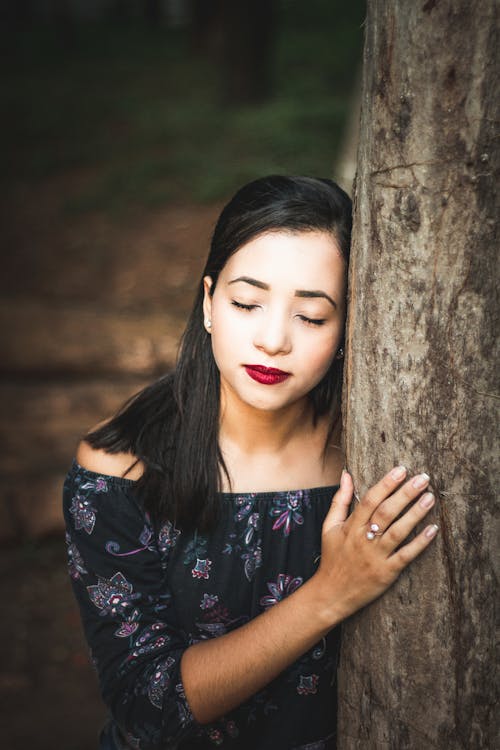Free Woman Wearing Black Floral Off-shoulder Top Leaning on Tree Trunk Stock Photo