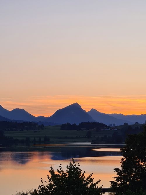 Free Tranquil lake with hills silhouetted against a vibrant sunset sky. Stock Photo