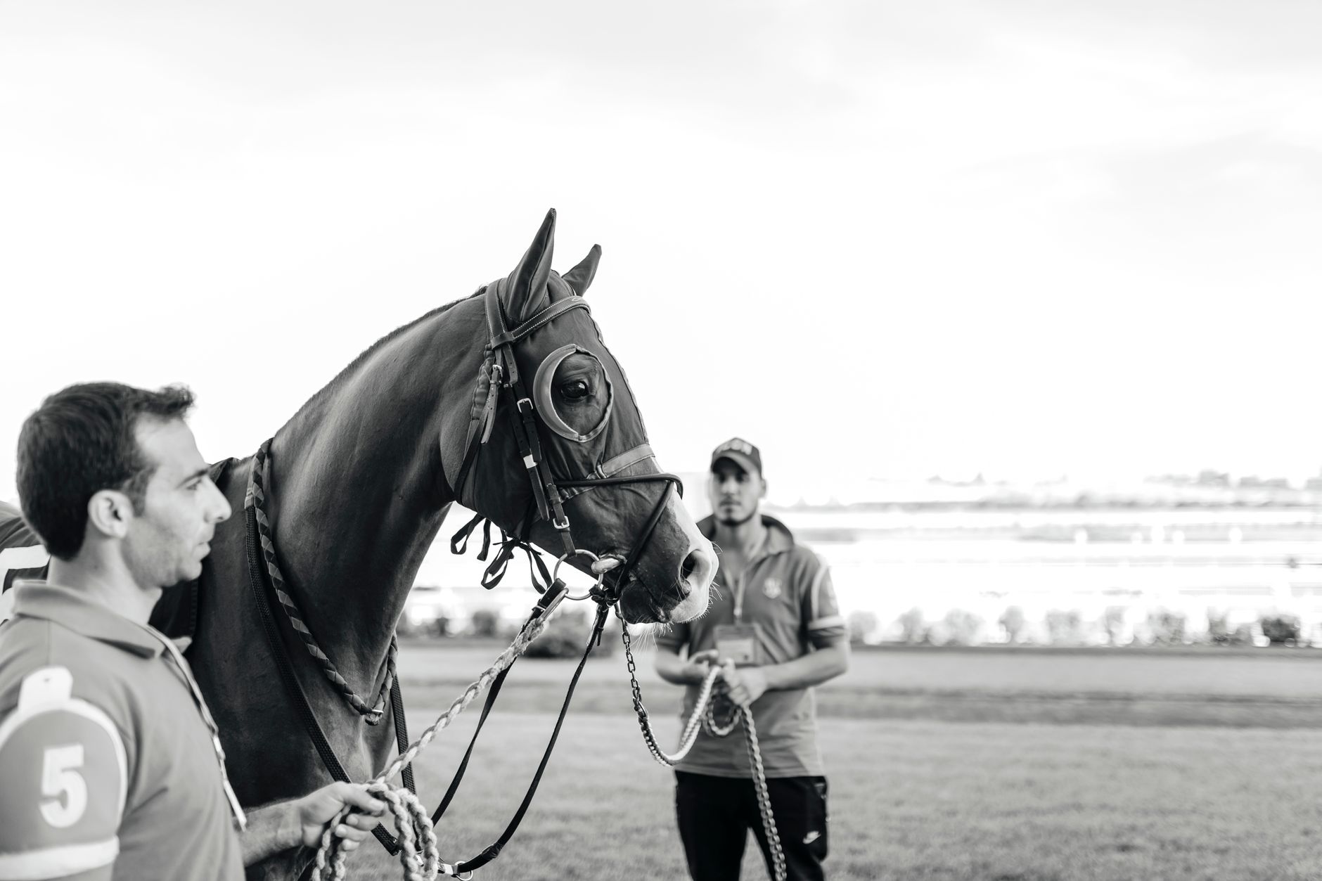 Two men preparing a racehorse for competition on a track.