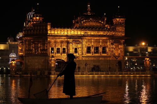 Free Illuminated Golden Temple in Amritsar captured against night sky with silhouette boater. Stock Photo