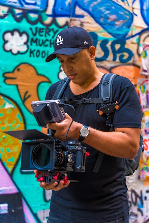 Man Looking at his Camera in Front of a Wall with Graffiti 