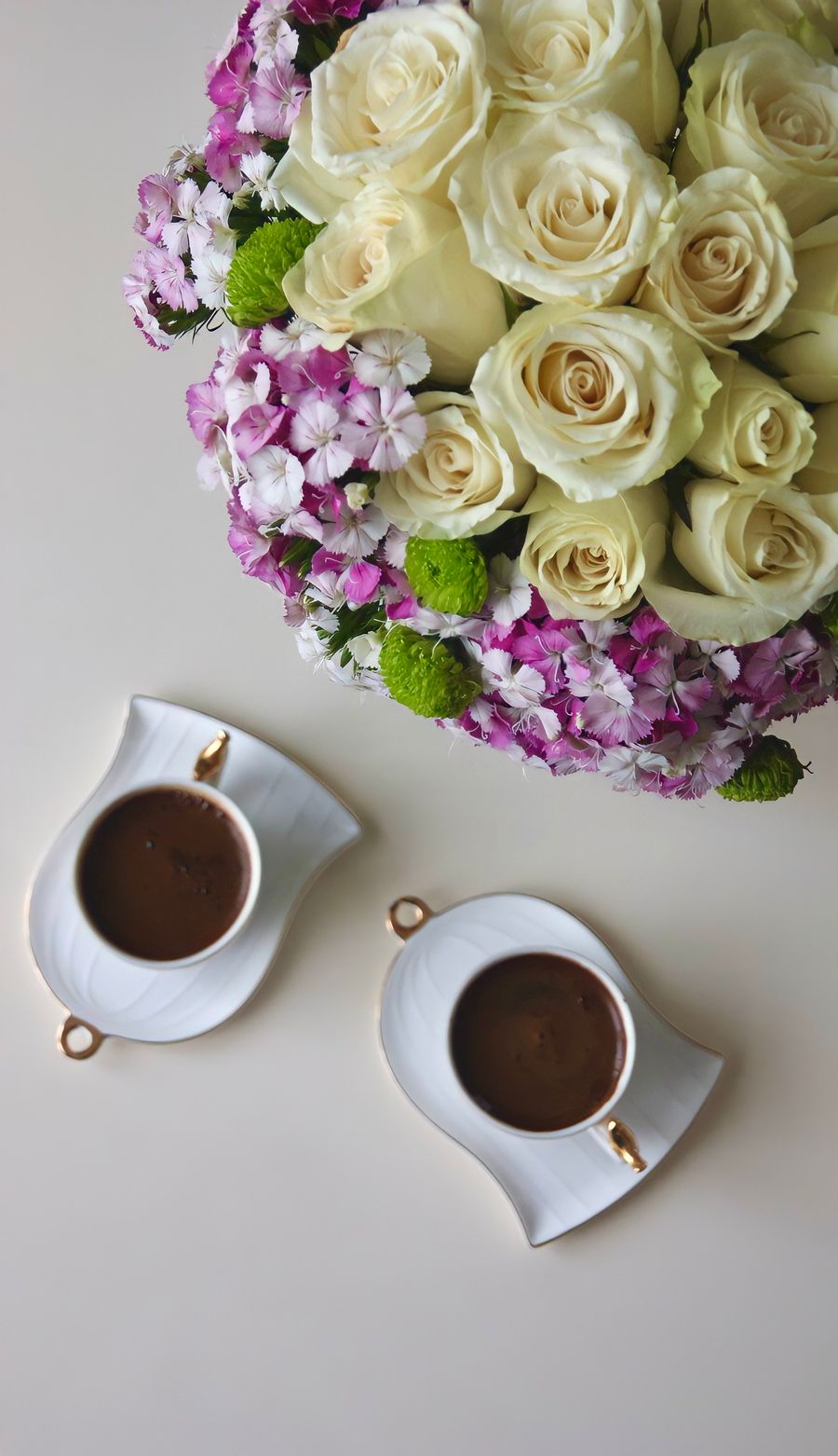 White roses beside two elegant coffee cups, styled from above