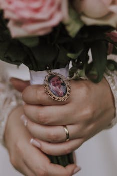 Close-up of a bride's hands holding a bouquet with a memorial charm, symbolizing love and remembrance.